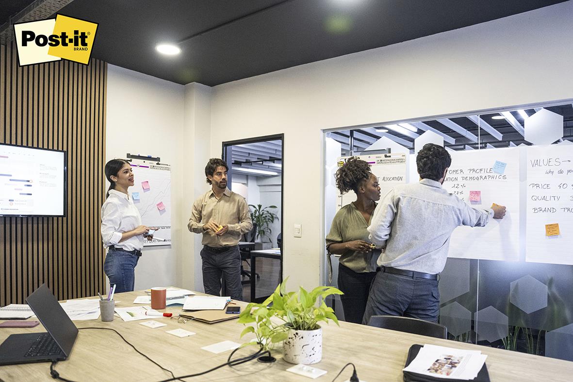 Grupp människor i ett mötesrum med blädderblock och Post-it lappar, arbetar tillsammans på en presentation eller brainstorming.
