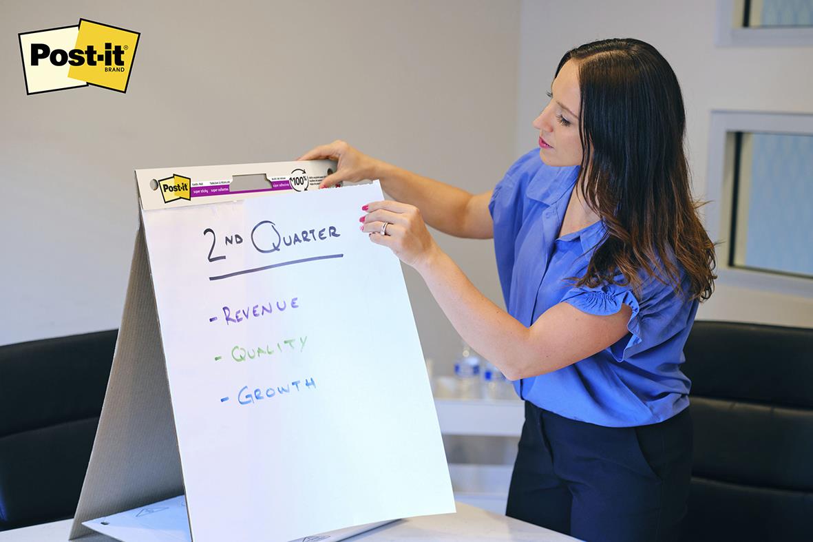 Kvinna skriver på en blädderblock med Post-it klisterlappar i ett kontorsrum