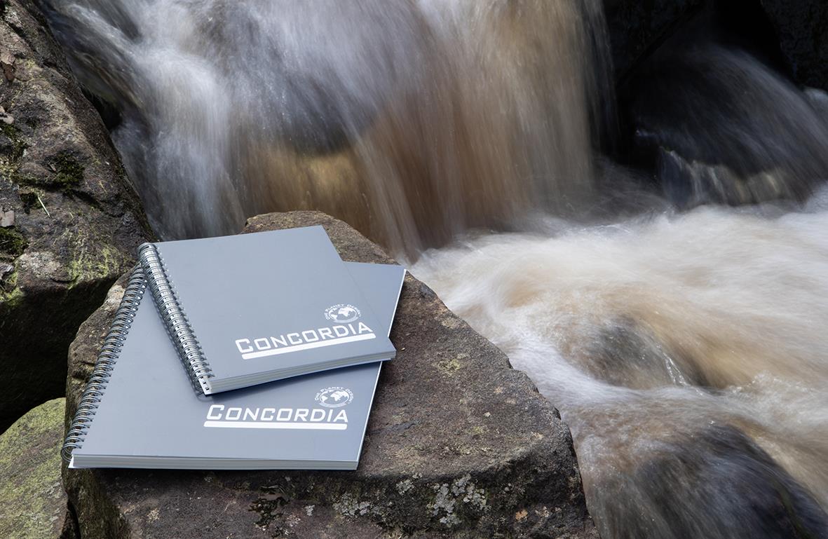 Anteckningsblock med linjerat papper från Hylte Eco Concordia, placerad vid en bäck