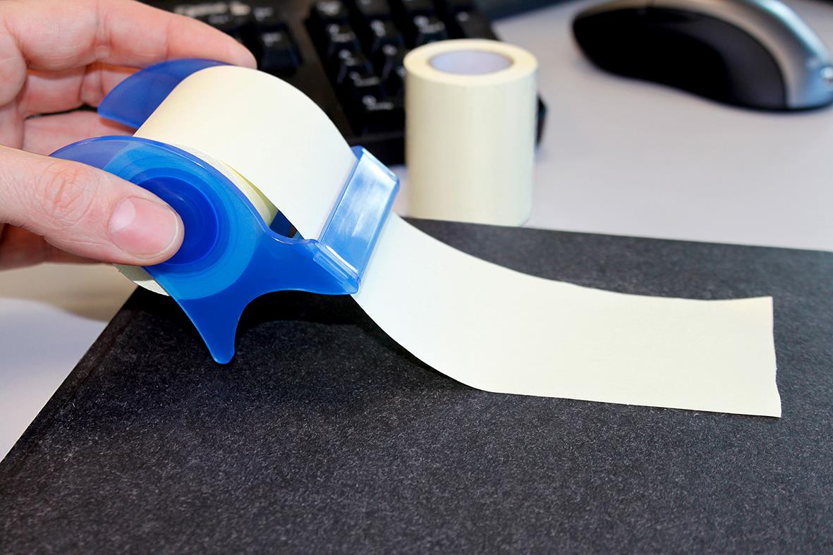 Person som använder en blå och vit tejp för att märka en svart yta, med extra tejp i bakgrunden