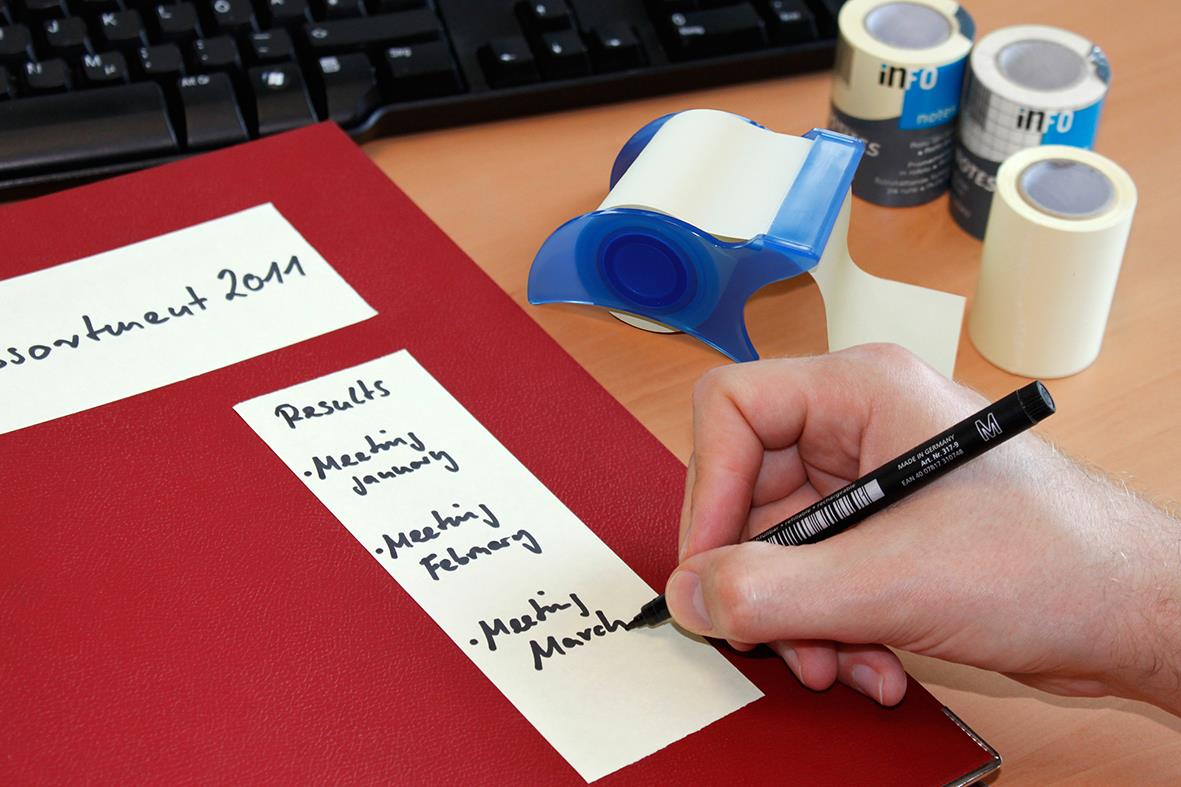 Person skriver på en whiteboard med memomurull och tejp i bakgrunden