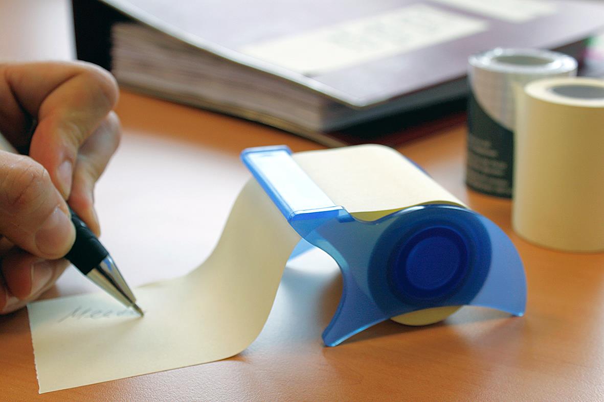 Gul notisblock med 10 meters tejp på skrivbord med papper och skrivredskap