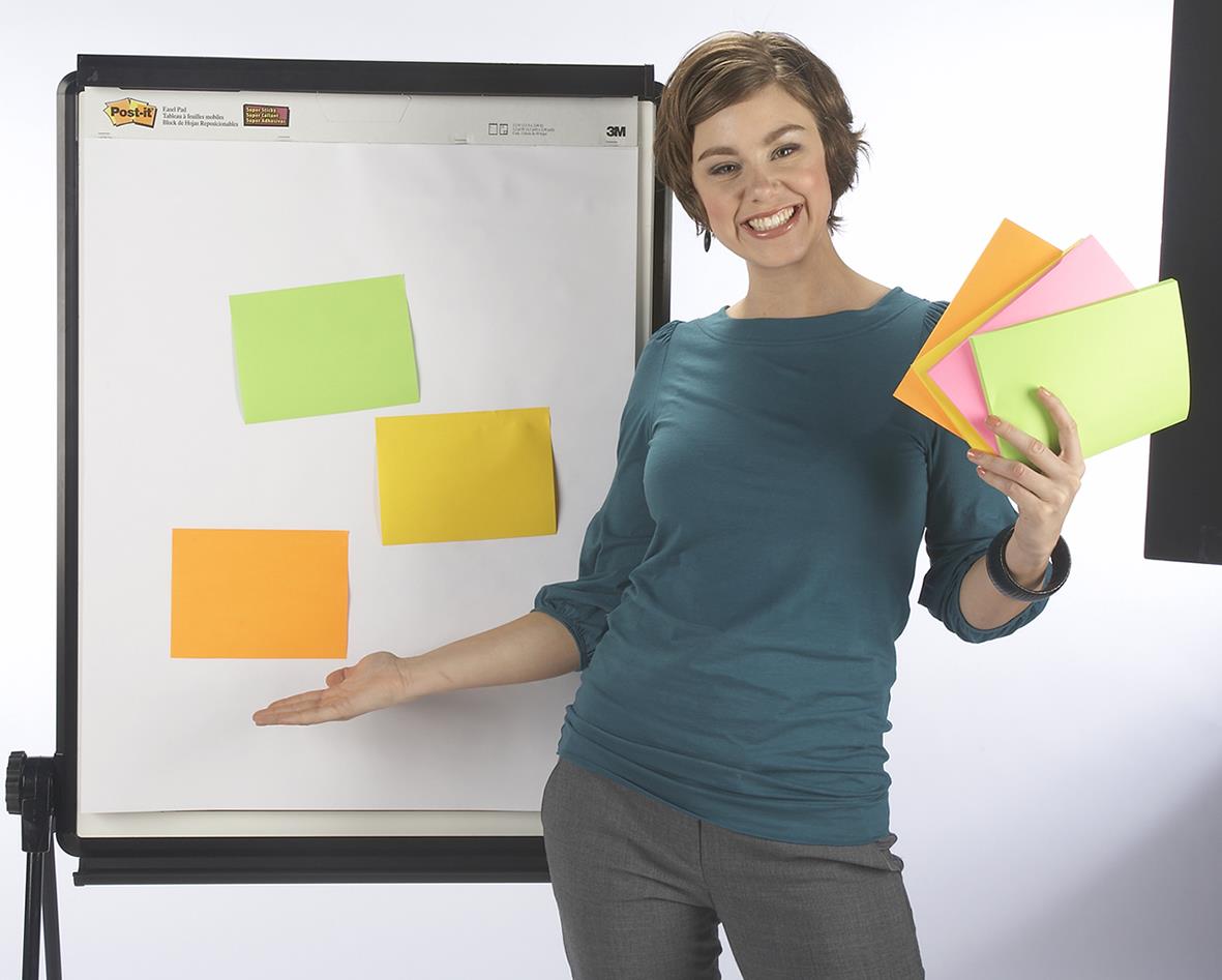 Glad kvinna håller färgglada Post-it lappar framför whiteboard med fler lappar