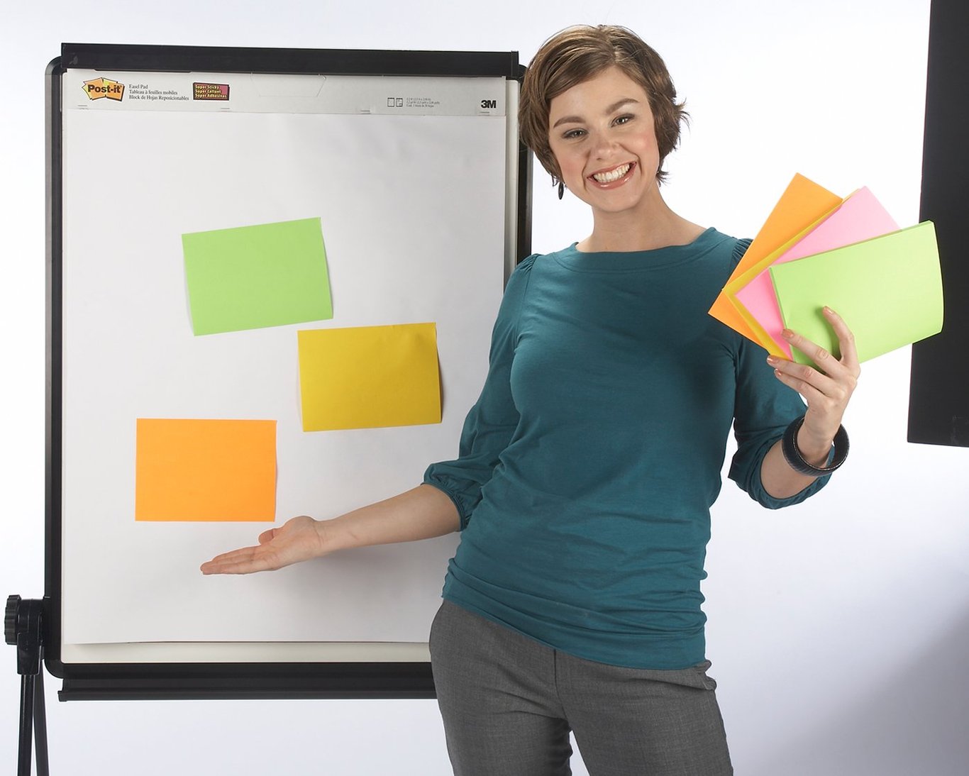 Glad kvinna håller färgglada Post-it lappar framför whiteboard med fler lappar