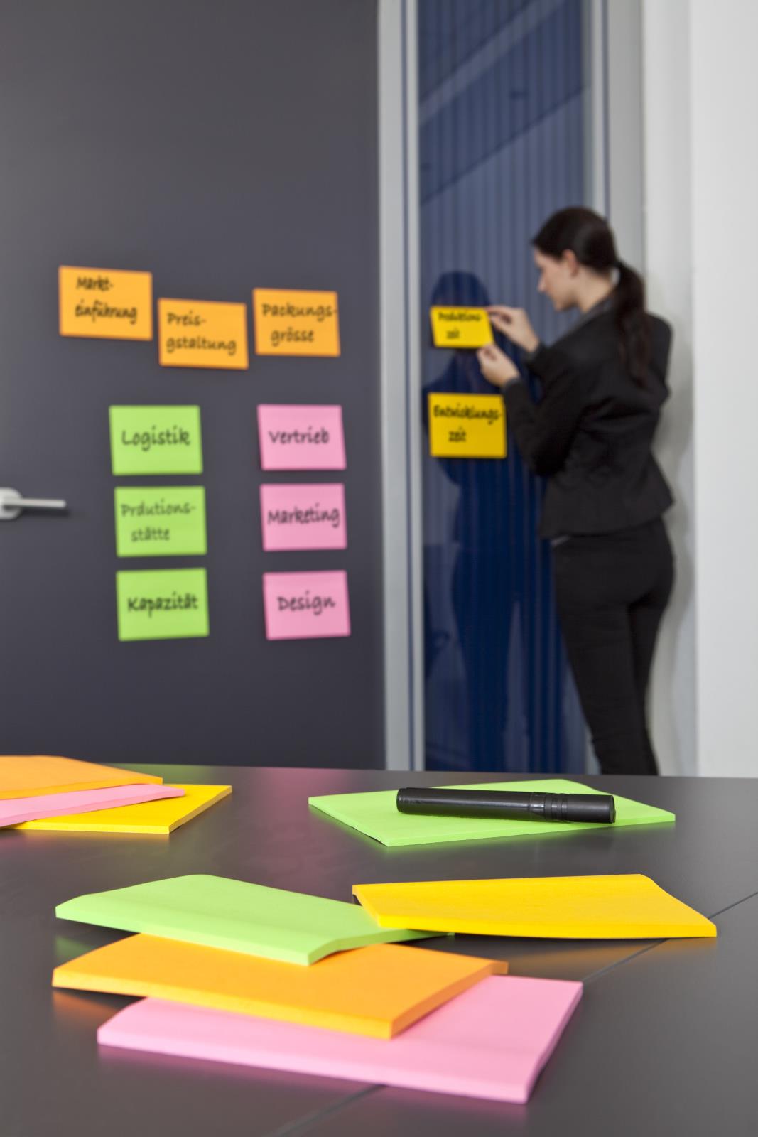 Kvinna sätter upp färgglada Post-it lappar på vägg i mötesrum med fler lappar på bordet