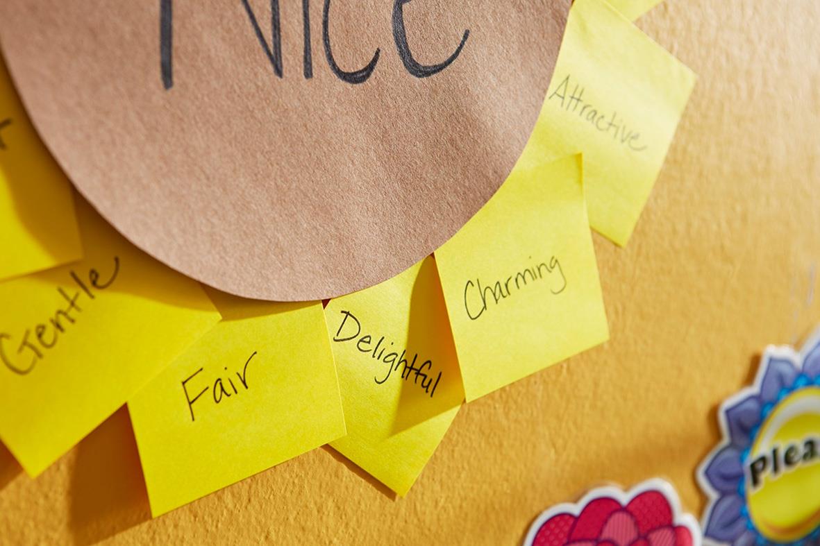 Hållare för Post-it-lappar med en gul Post-it och ord som Fair, Delightful, Charming, Nice, Gently på en vägg