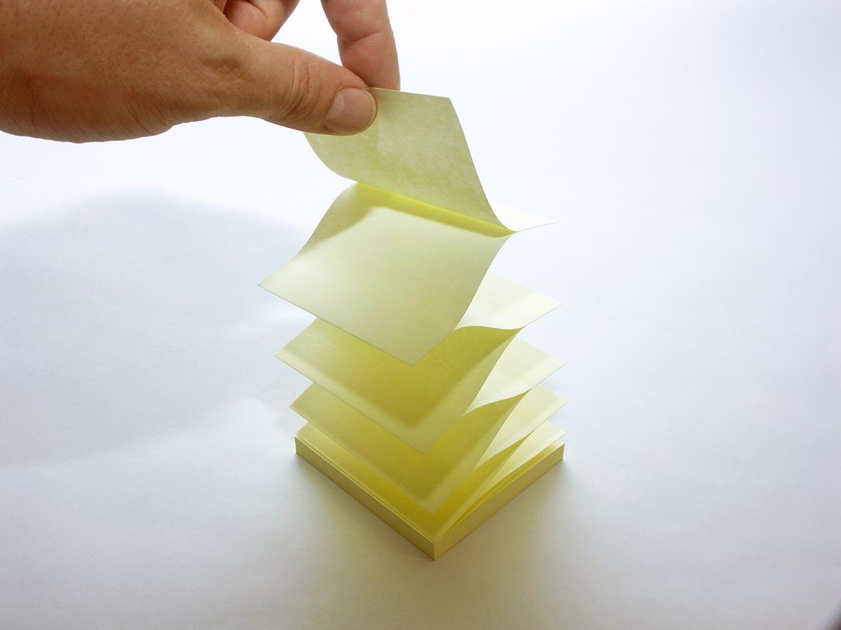 Hand som tar bort en gul Post-it-lapp från en stapel av likadana lappar