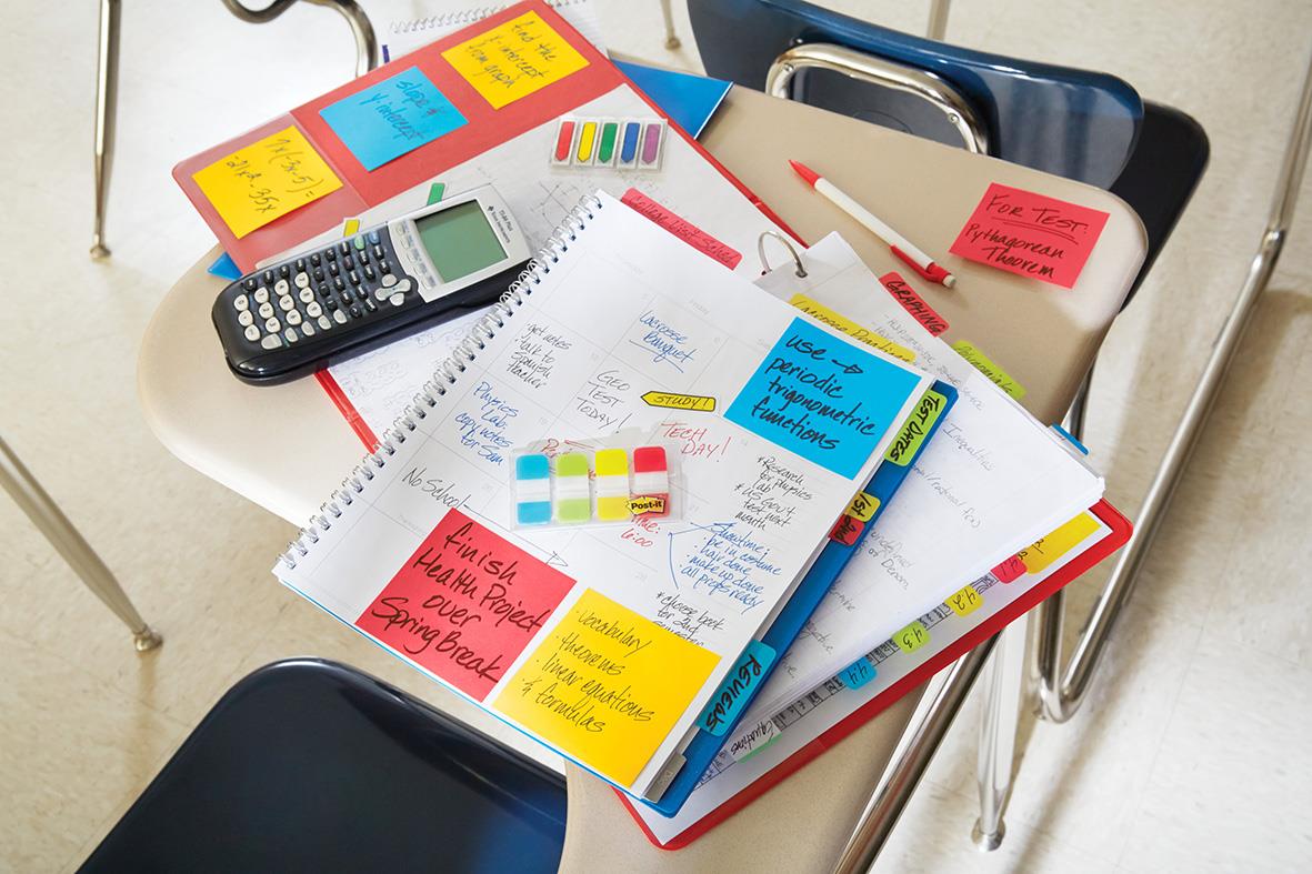 Stökigt skrivbord med Post-it lappar, papper, penna och miniräknare på en vit bord