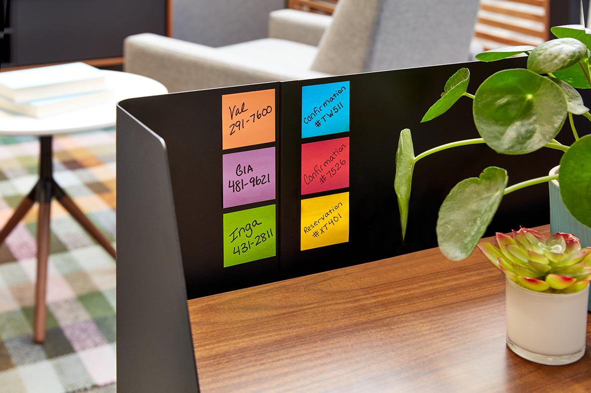 Post-it notisar med färgglada klisterlappar på en svart väggavdelare vid ett skrivbord