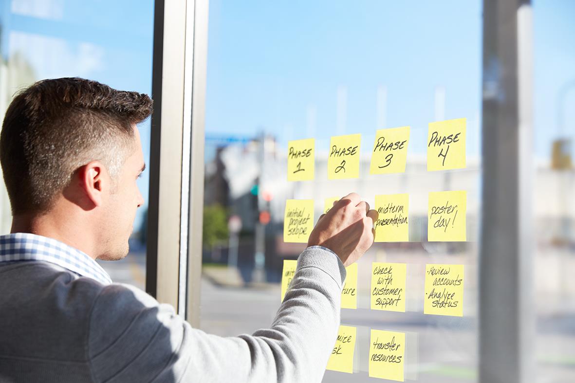Man placerar gula Post-it lappar på ett fönster för planering eller påminnelser