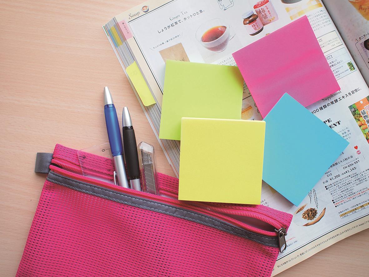 Färgglada post-it lappar i neonfärger på ett bord med pennor och en öppen tidning