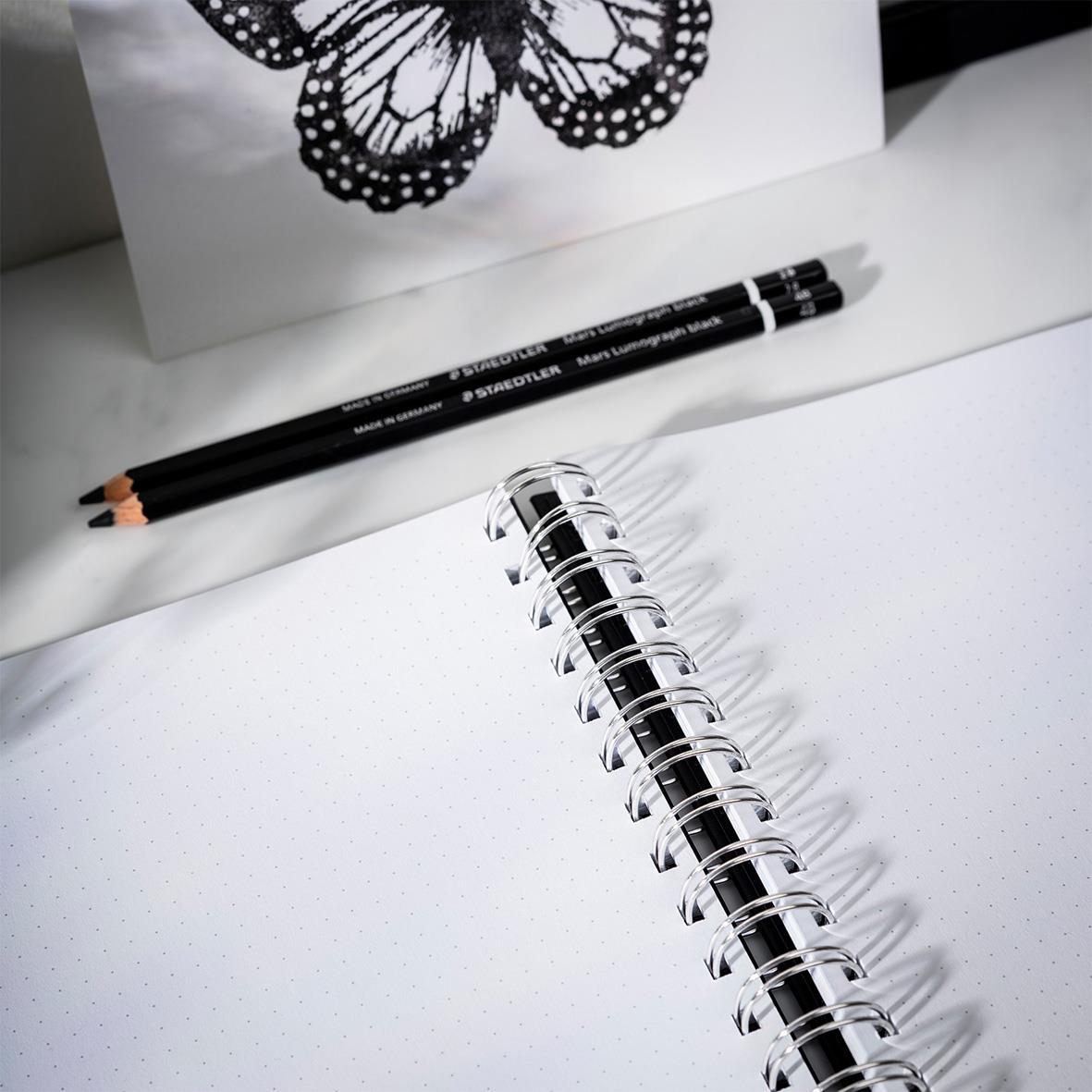 Svart anteckningsbok med spiralbindning och tomma sidor, två pennor bredvid