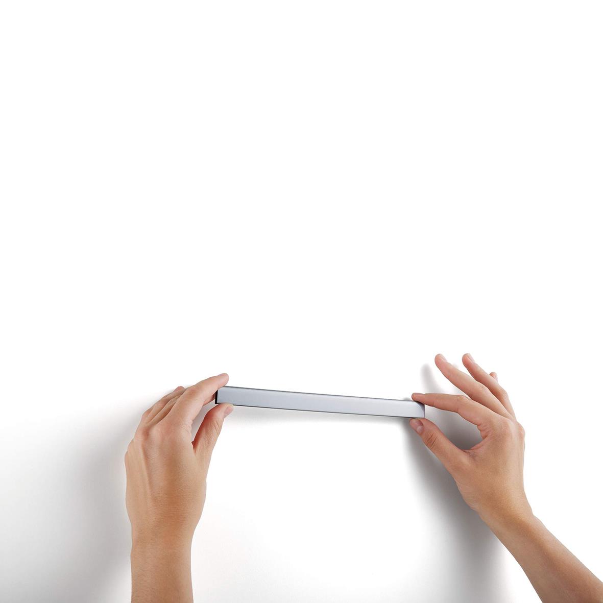 Person som håller en magnetisk pappershållare i silver mot en vit vägg