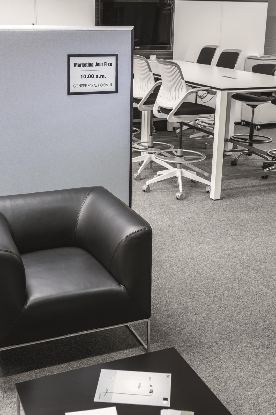 Svart Duraframe grip A4 informationsskylt i kontorsmiljö med konferensrum och möbler