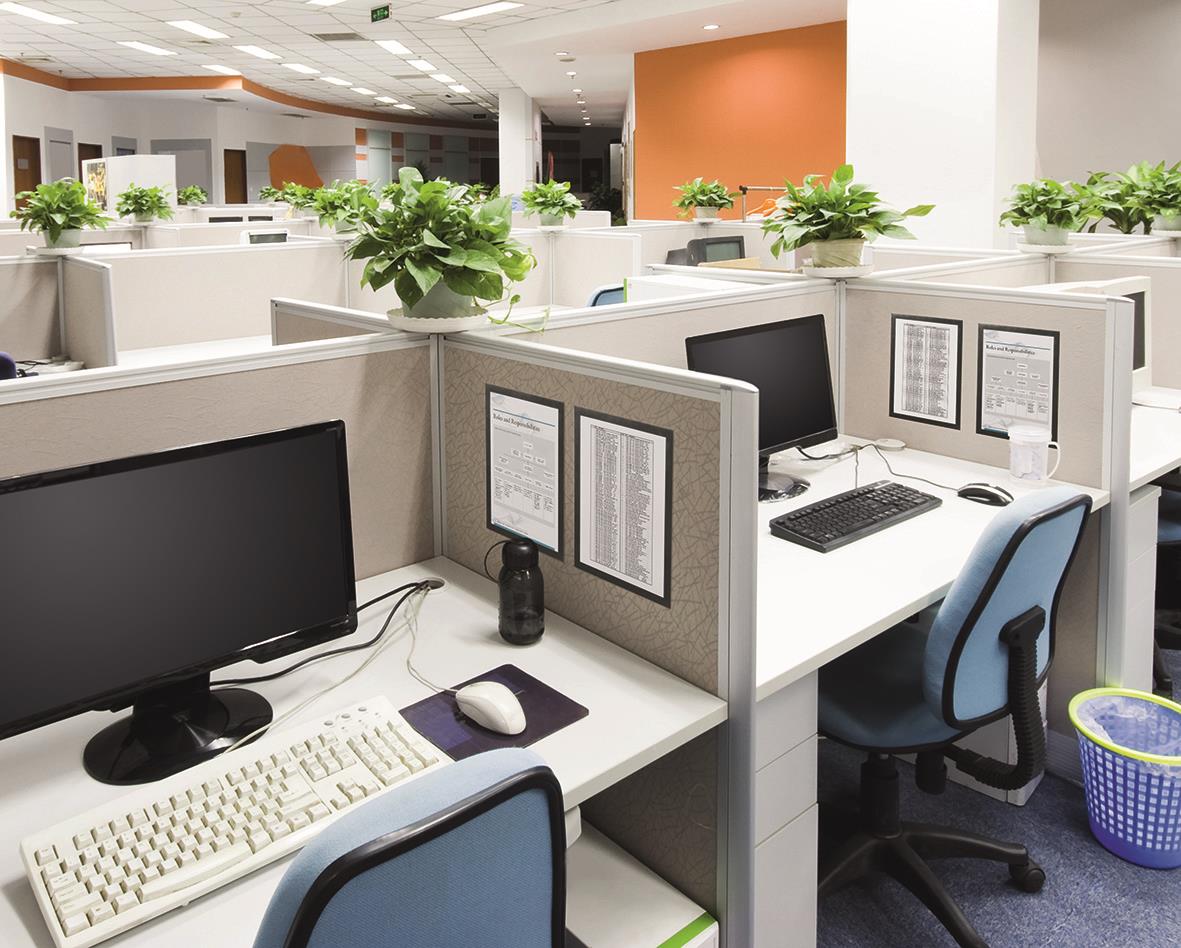 Kontorslandskap med skrivbord, datorer, växter och avskärmningspaneler i ett öppet kontorsutrymme