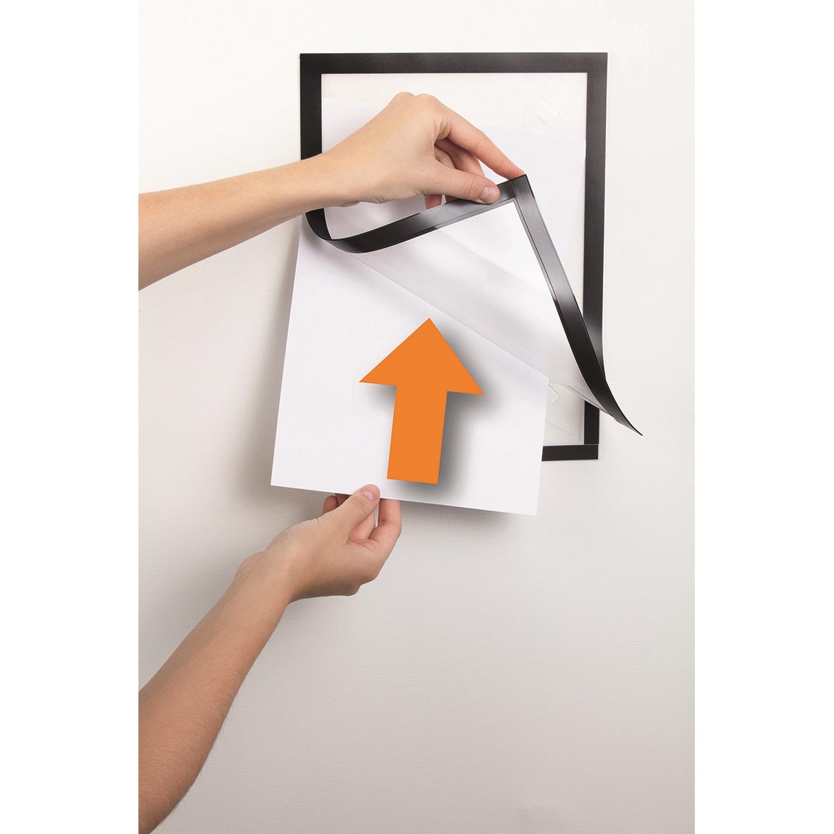 Person som sätter upp svart Duraframe väggram med svart tejp på en vit vägg, visar hur man fäster en A4-size poster