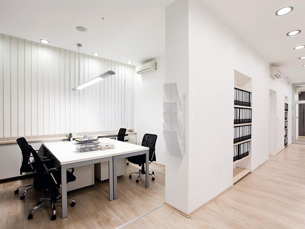 Modern kontorsrum med skrivbord, stolar och hyllor med pärmar i en ljus, minimalistisk miljö