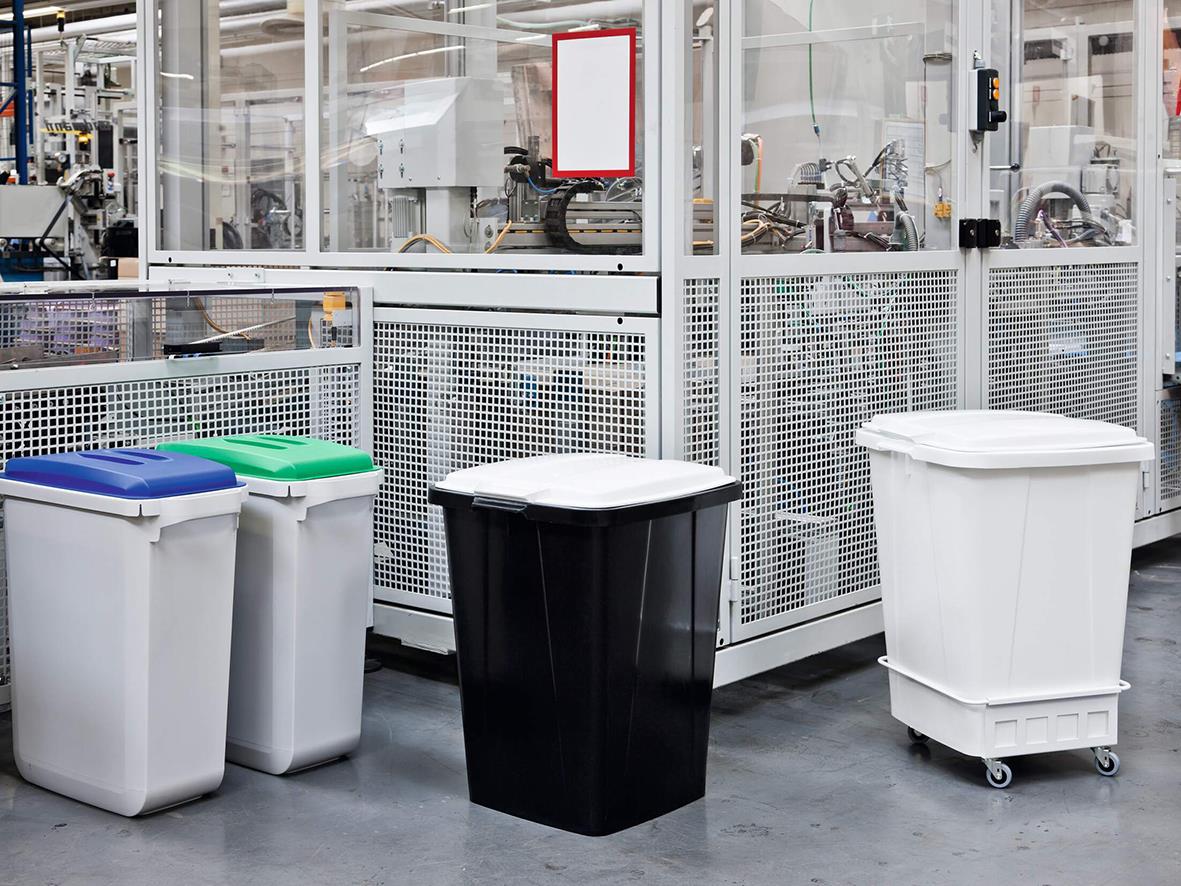 Fyra återvinningskärl i olika färger och storlekar i industriell miljö