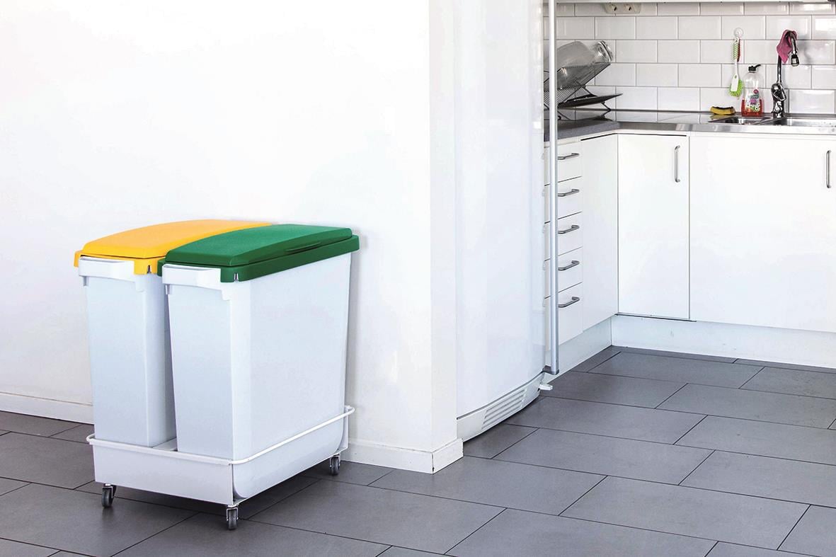Två papperskorgar i plast, en gul och en grön, placerade i ett kök med vita skåp och grått golv