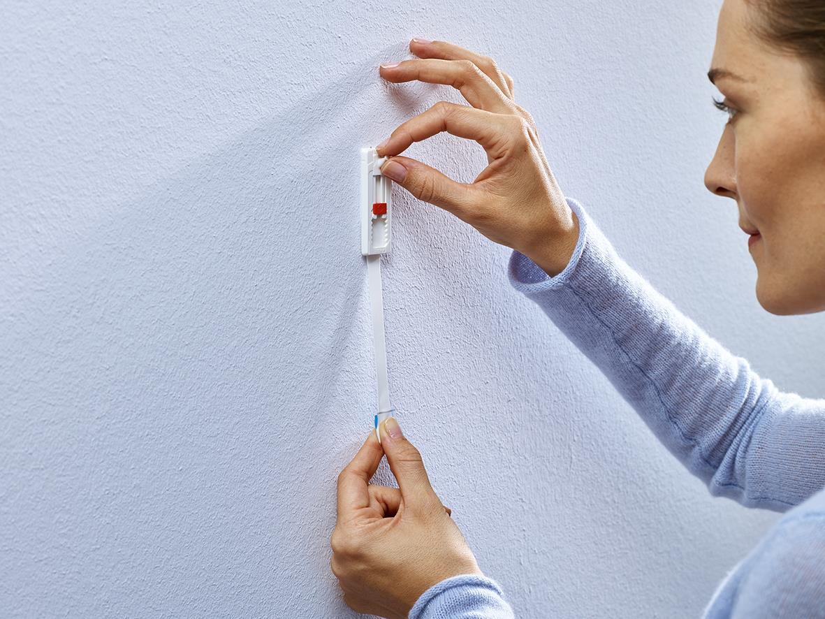 Kvinna applicerar självhäftande Tesa Powerstrips på vägg för att hänga upp något