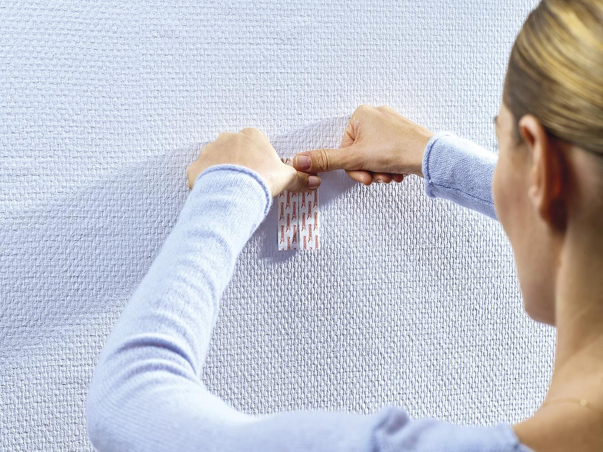 Kvinna fäster Tesa Powerstrips på vägg för att hänga upp något