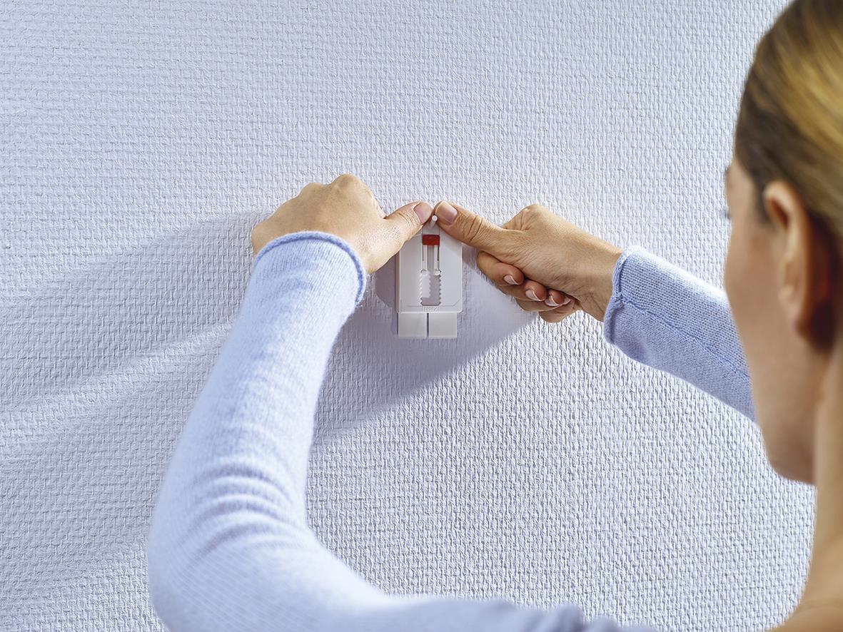 Person fäster Tesa Powerstrips på vägg för att hänga upp något