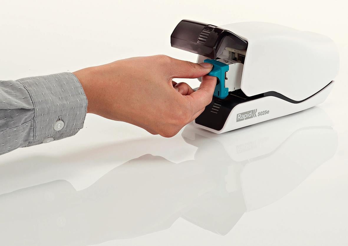 Person som laddar en Rapid 5025E klamphäftapparat med vita ark i bakgrunden