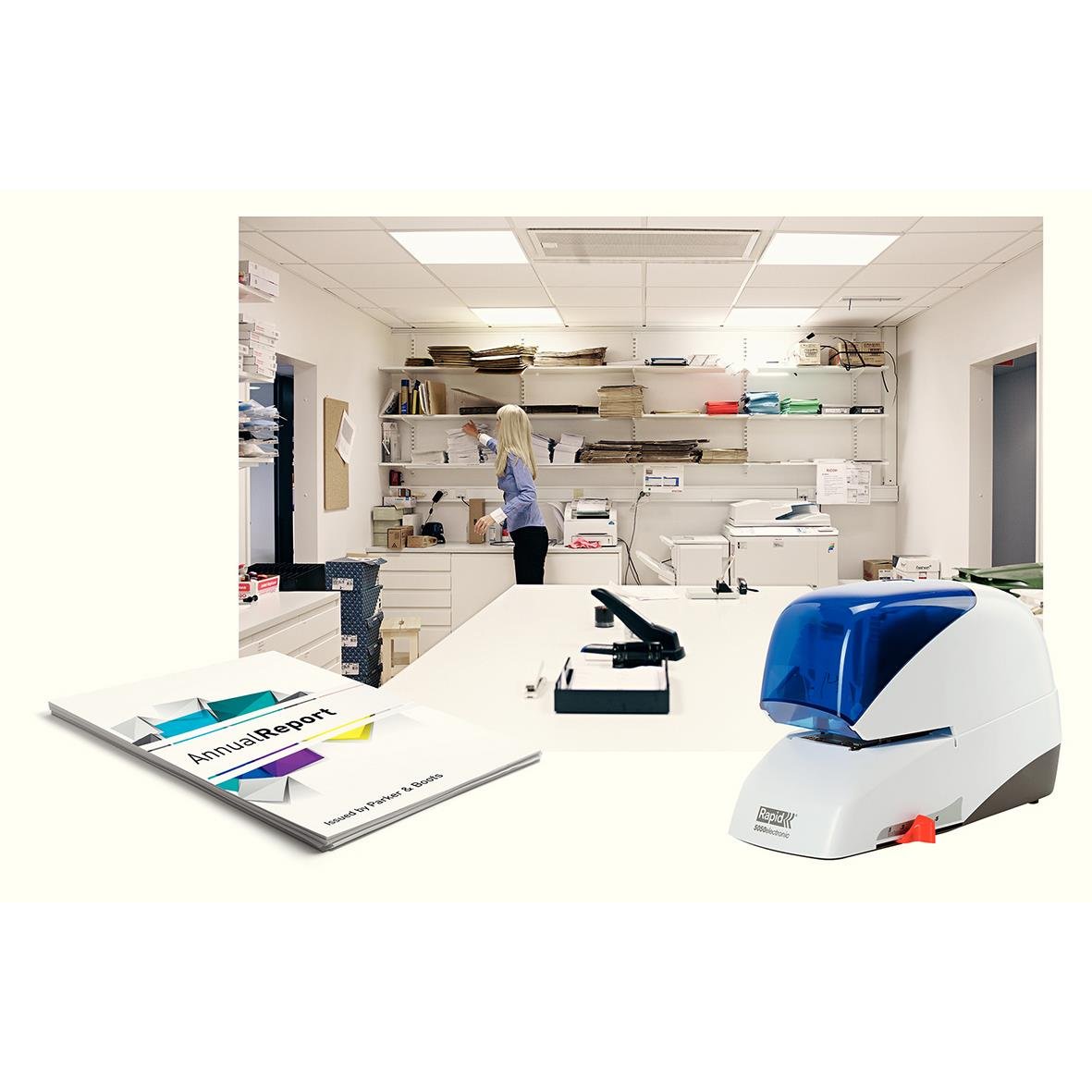 Kontorsmiljö med en person som arbetar vid skrivbord och en blå elhäftare på bordet