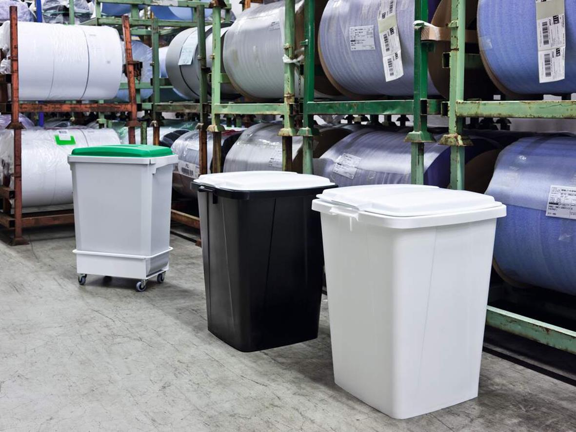 Tre återvinningskärl med lock i grå, svart och vit färg i lagerlokal