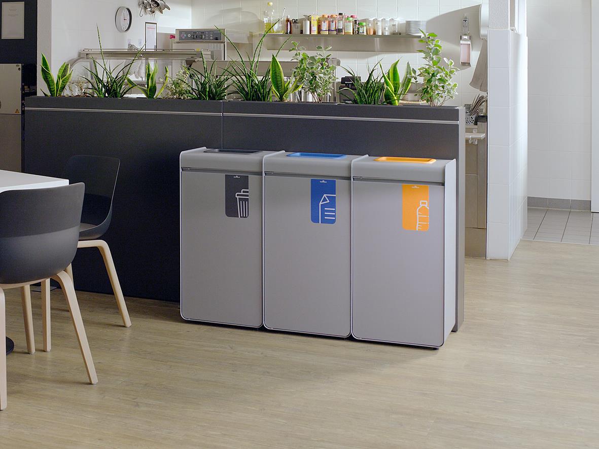 Tre återvinningskärl i grått, blått och orange för sortering i kök eller kontor