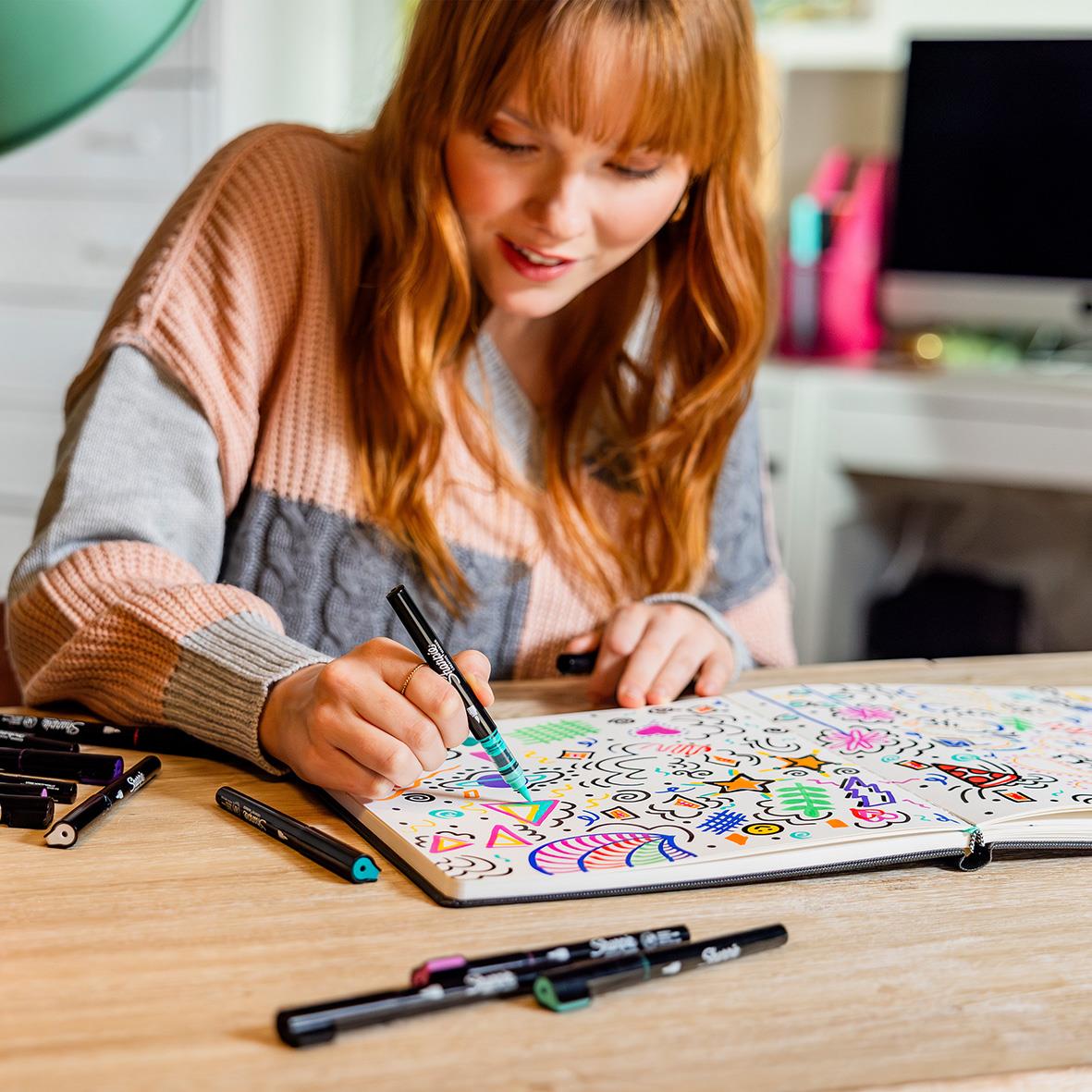 Ung kvinna som ritar och färglägger på en stor whiteboard med olika färgglada markörer