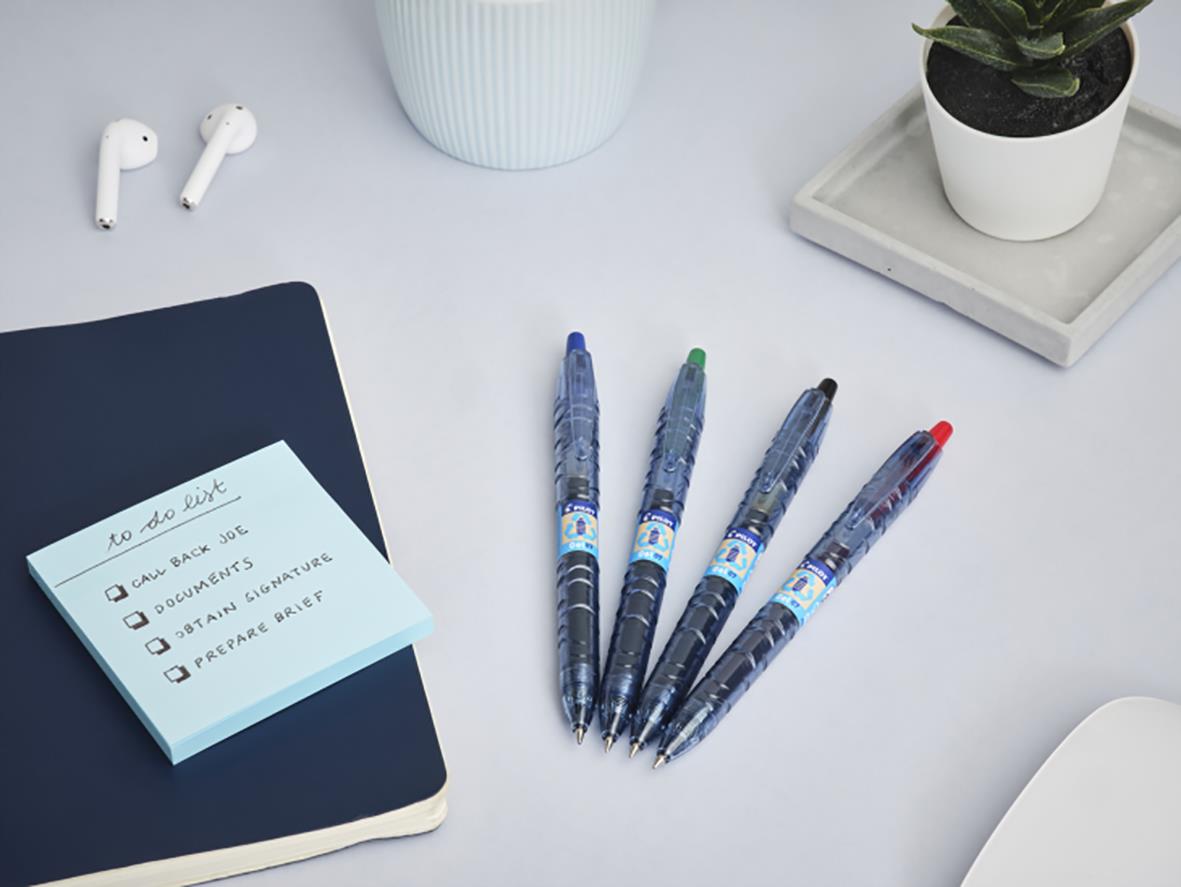 Fyra Pilot B2P Ecoball Begreen kulspetspennor i olika färger på ett skrivbord med anteckningsblock, växt och hörlurar