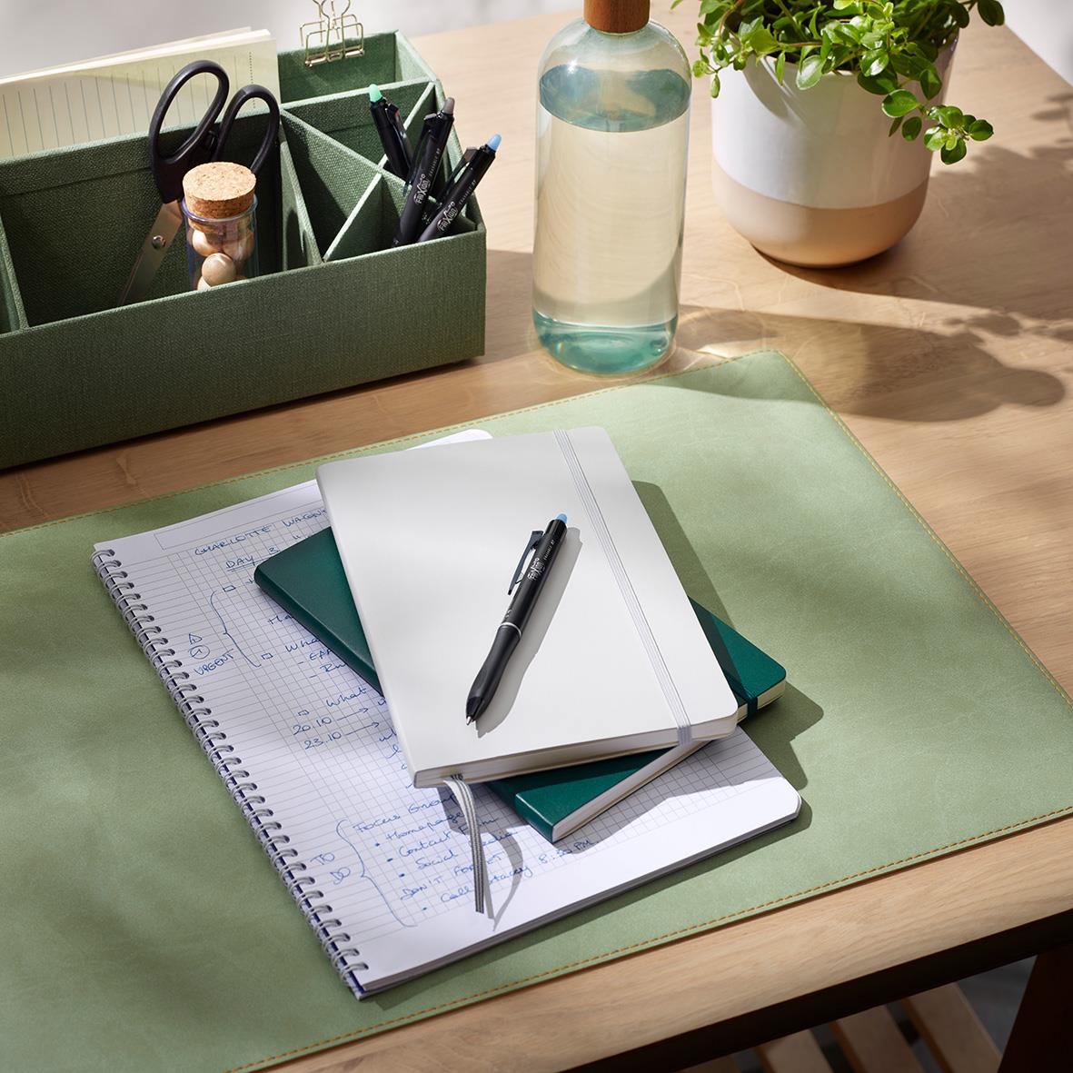 Skrivbord med anteckningsböcker, penna, växt och förvaringslåda med kontorsmaterial