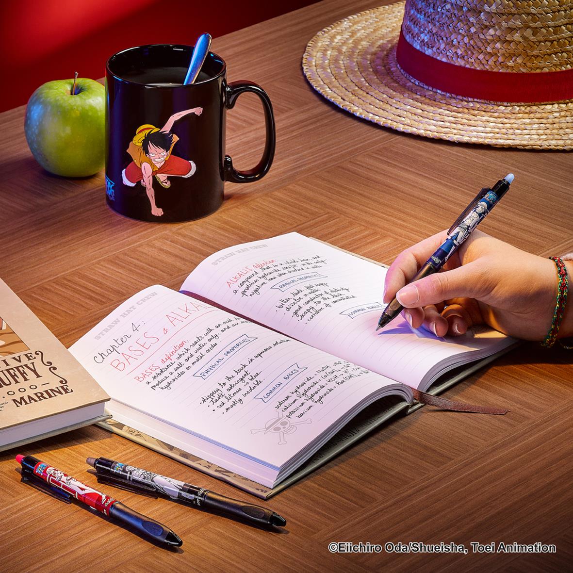 Svart Pilot Frixion Ball Plus One Piece kulspetspenna skrivs i anteckningsbok på träbord med kopp, äpple och solhatt i bakgrunden