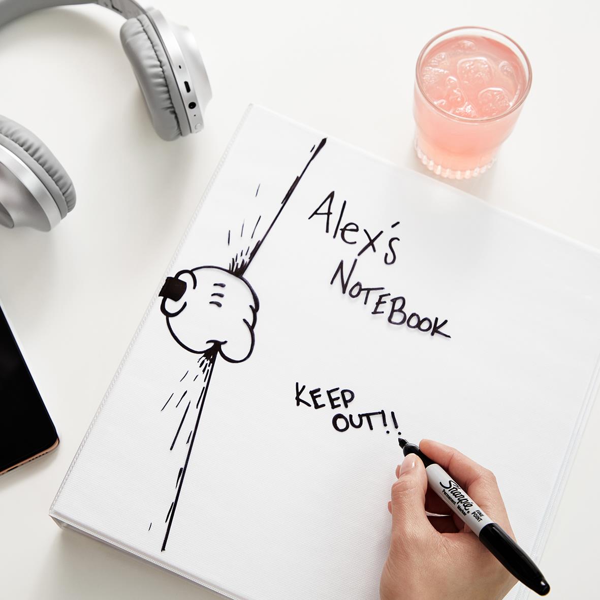 En hand skriver med en svart Sharpie på en anteckningsbok med en tecknad kanin och texten Alexis Notebook Keep Out
