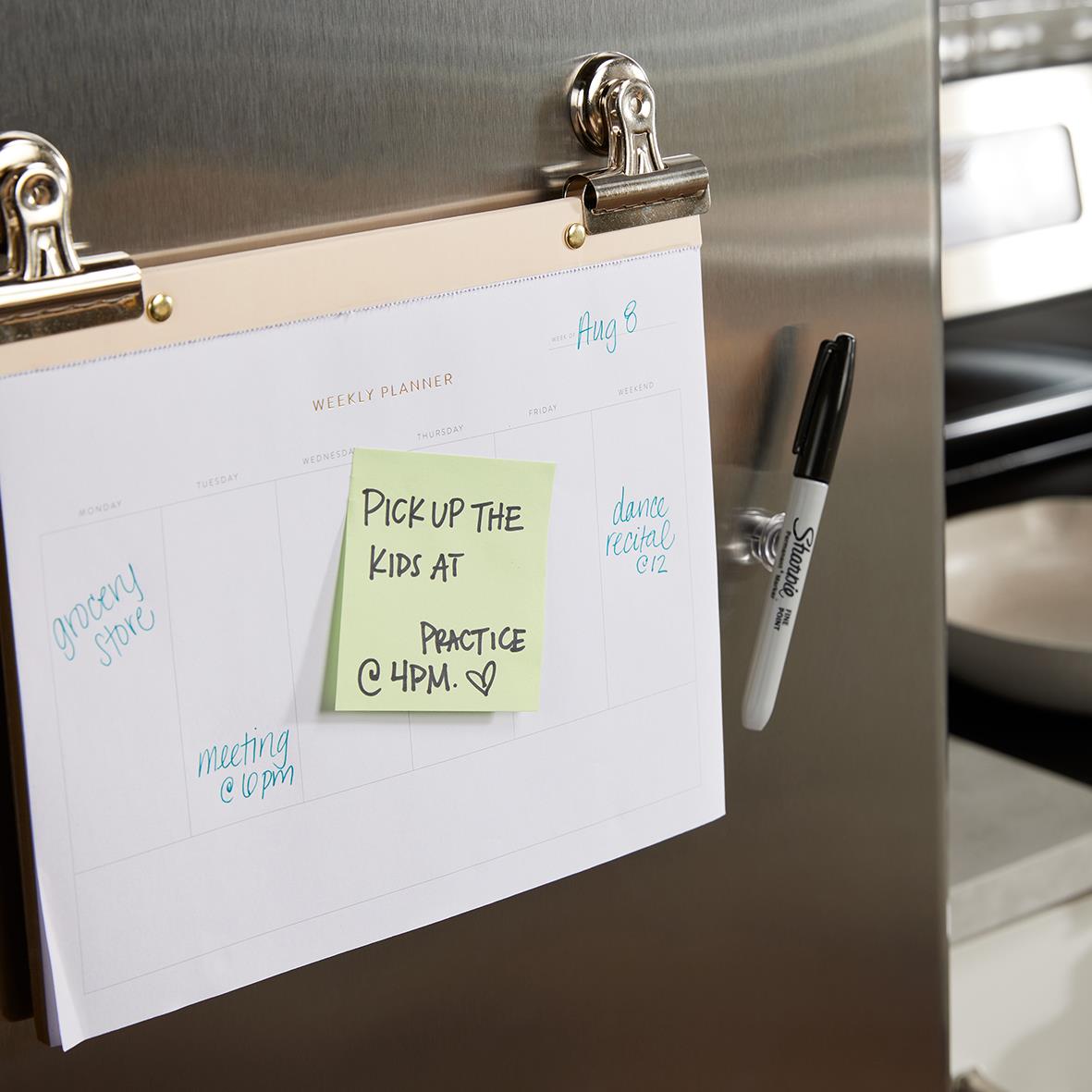 Svart Sharpie penna fäst på kylskåp med whiteboard och kalender, samt en post-it med anteckning