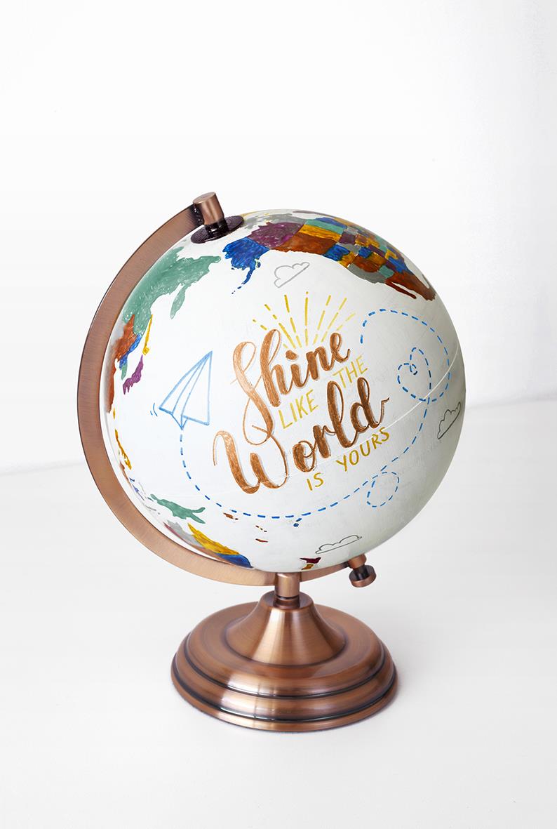 Globus med världskarta och texten Shine like the world is yours, på en kopparfärgad bas