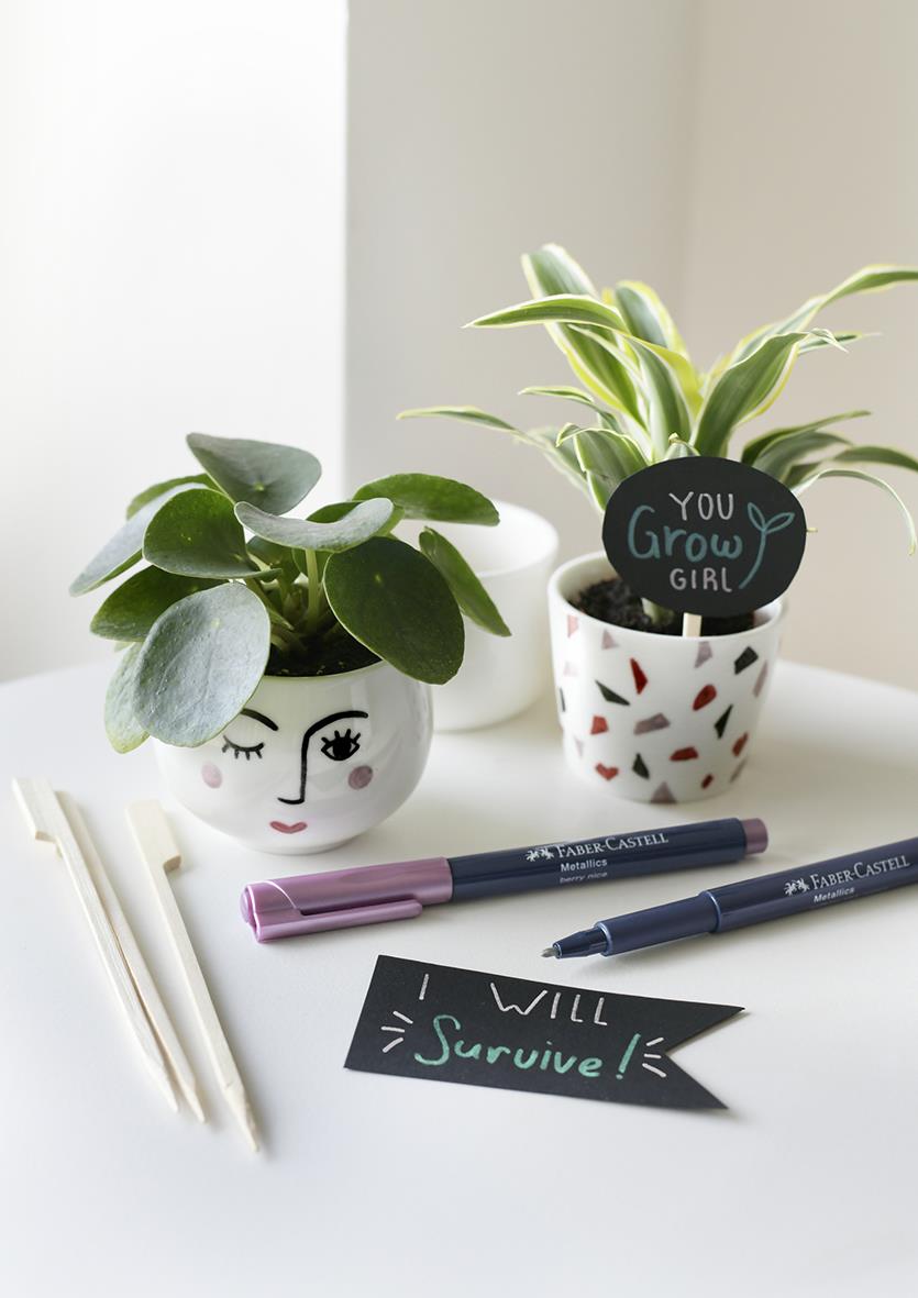 Två växter i dekorativa krukor, Faber-Castell metallics marker, ett svart lappar med text I Will Survive, vita pinnar