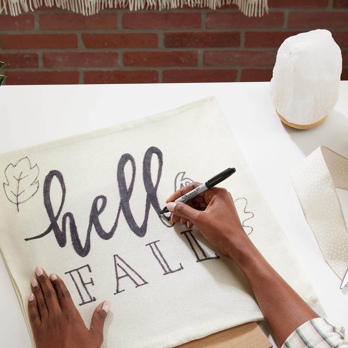 Person skriver med svart Sharpie permanent penna på tyg, ordet hello och andra bokstäver