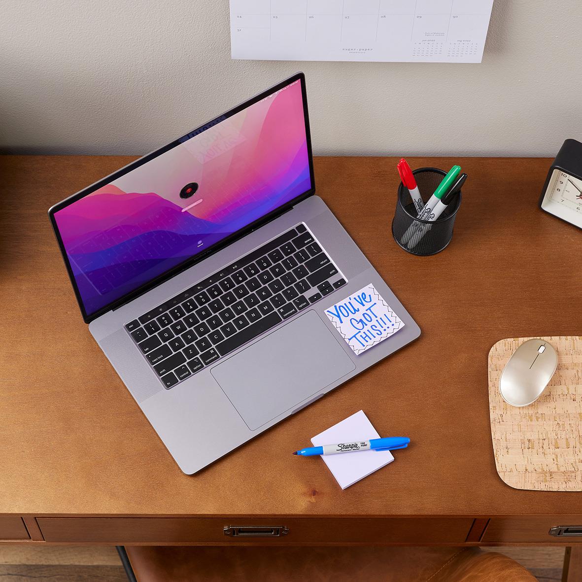 Laptop på skrivbord med pennor, papper och mus i närheten