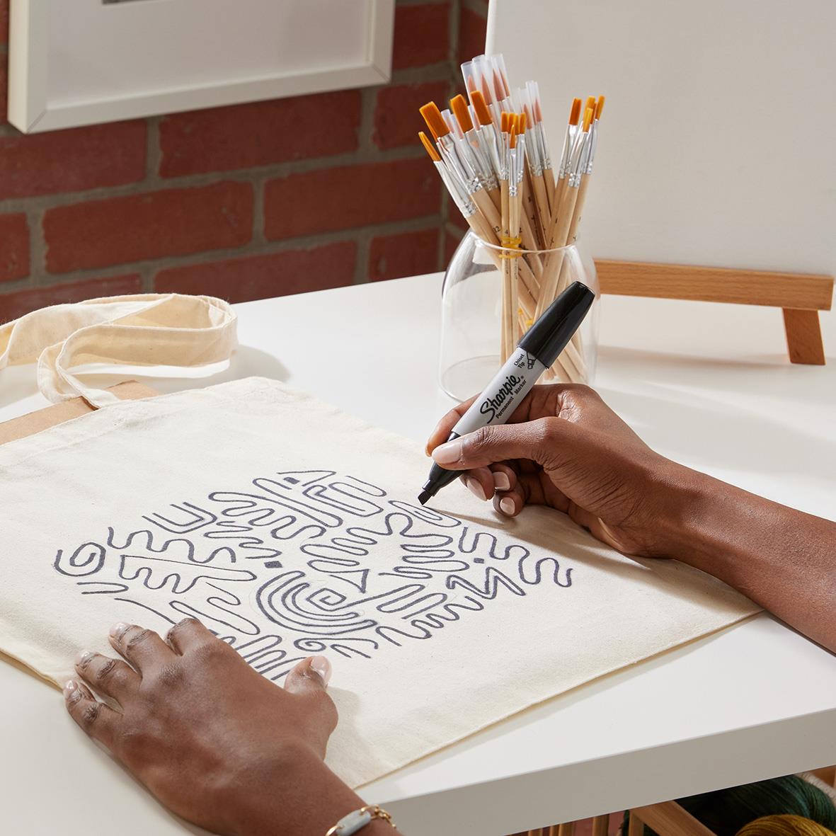 Person ritar ett mönster på en tygpåse med en svart permanent marker