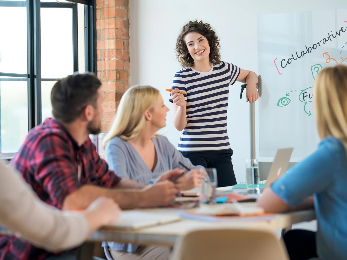 Kvinna som håller presentation framför grupp i konferensrum med whiteboard