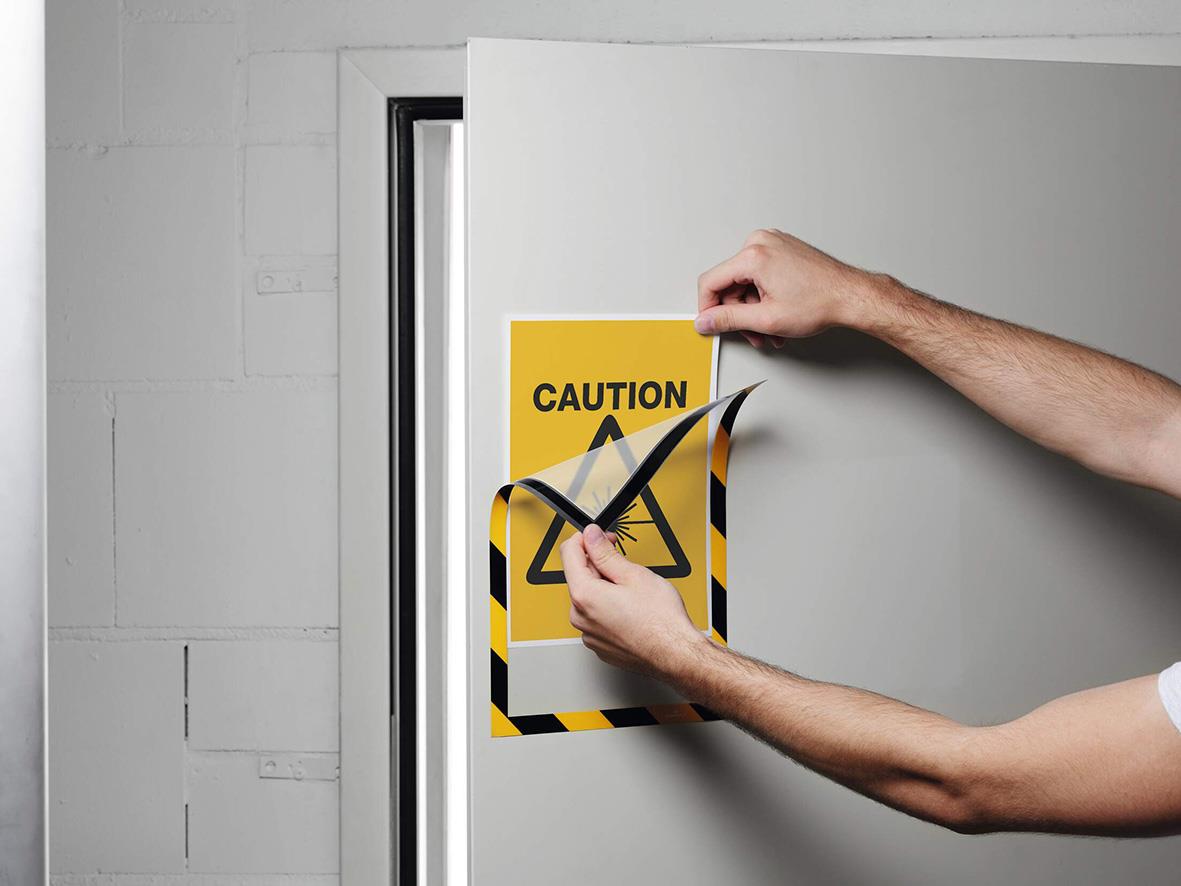 Person byter ut en varningsskylt på en vit dörr, gul och svart med texten CAUTION