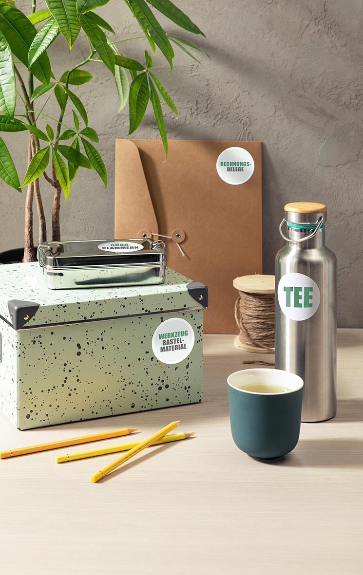 Rund etikett Avery L3416 Ø60mm på olika föremål som termos, kopp och förvaringslåda i ett hem- eller kontorsmiljö.