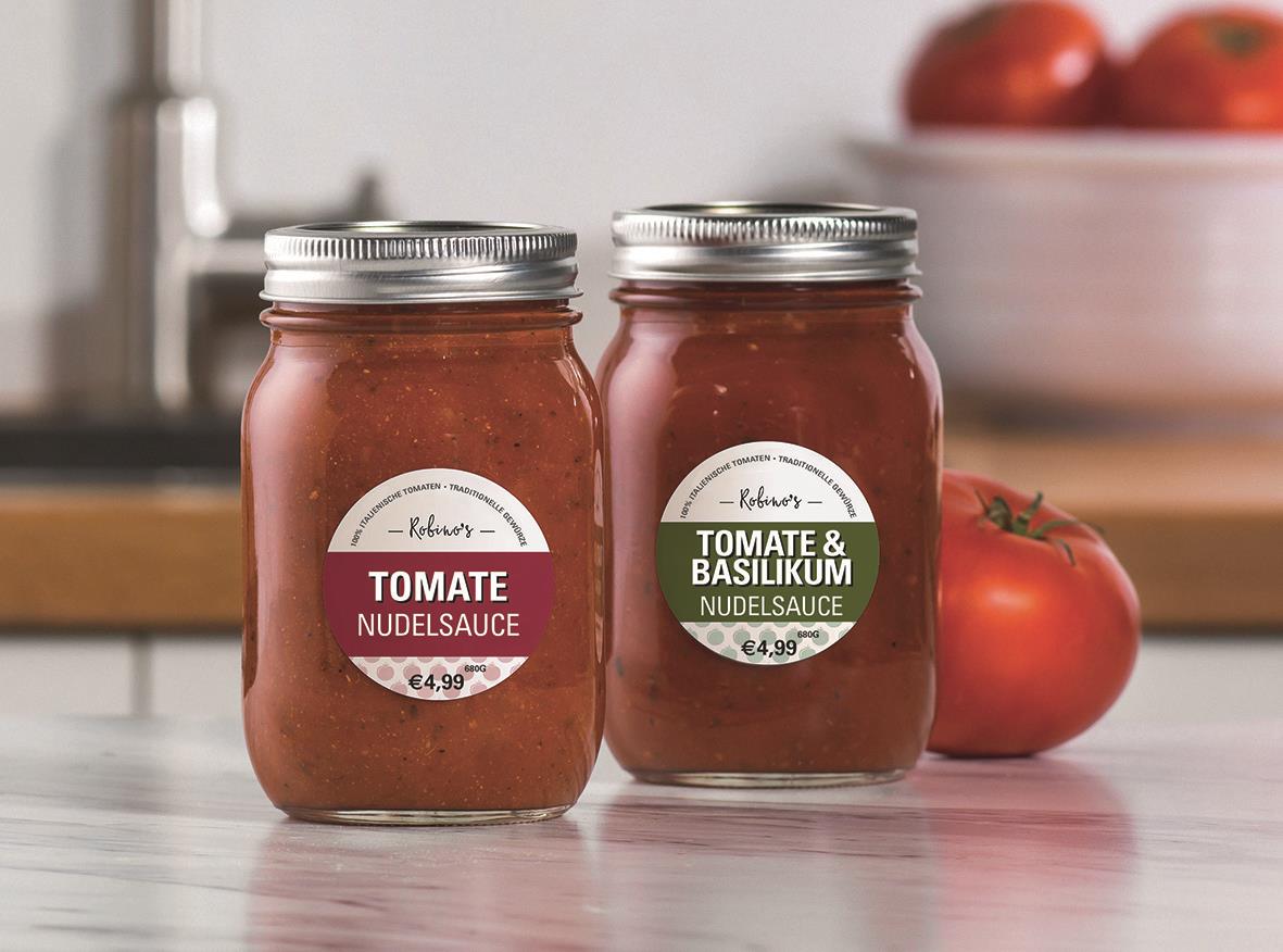 Två burkar med tomatsås på köksbänk, en med basilika och en utan, framför tre tomater