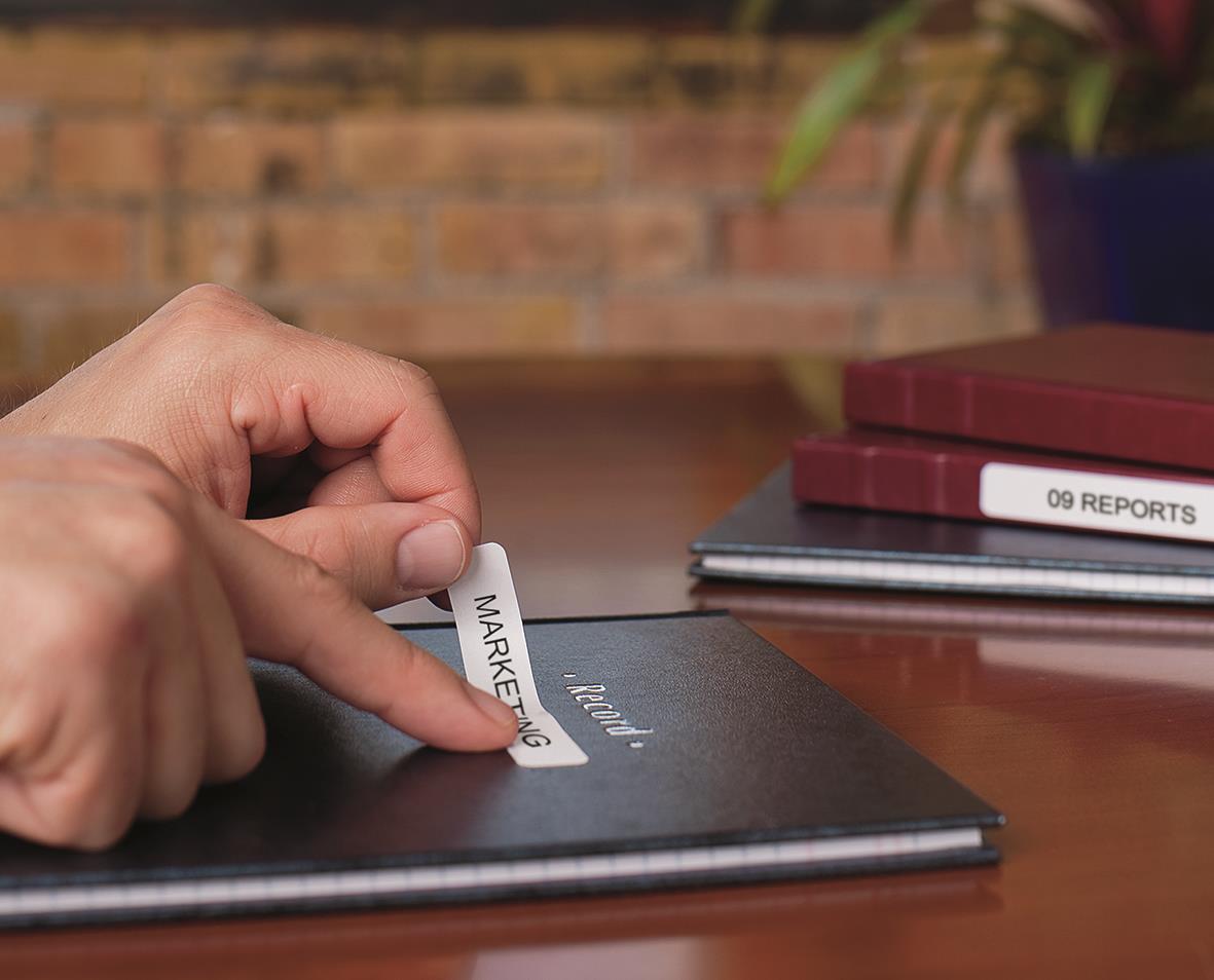 Person fäster en vit Dymo etikett på en svart mapp