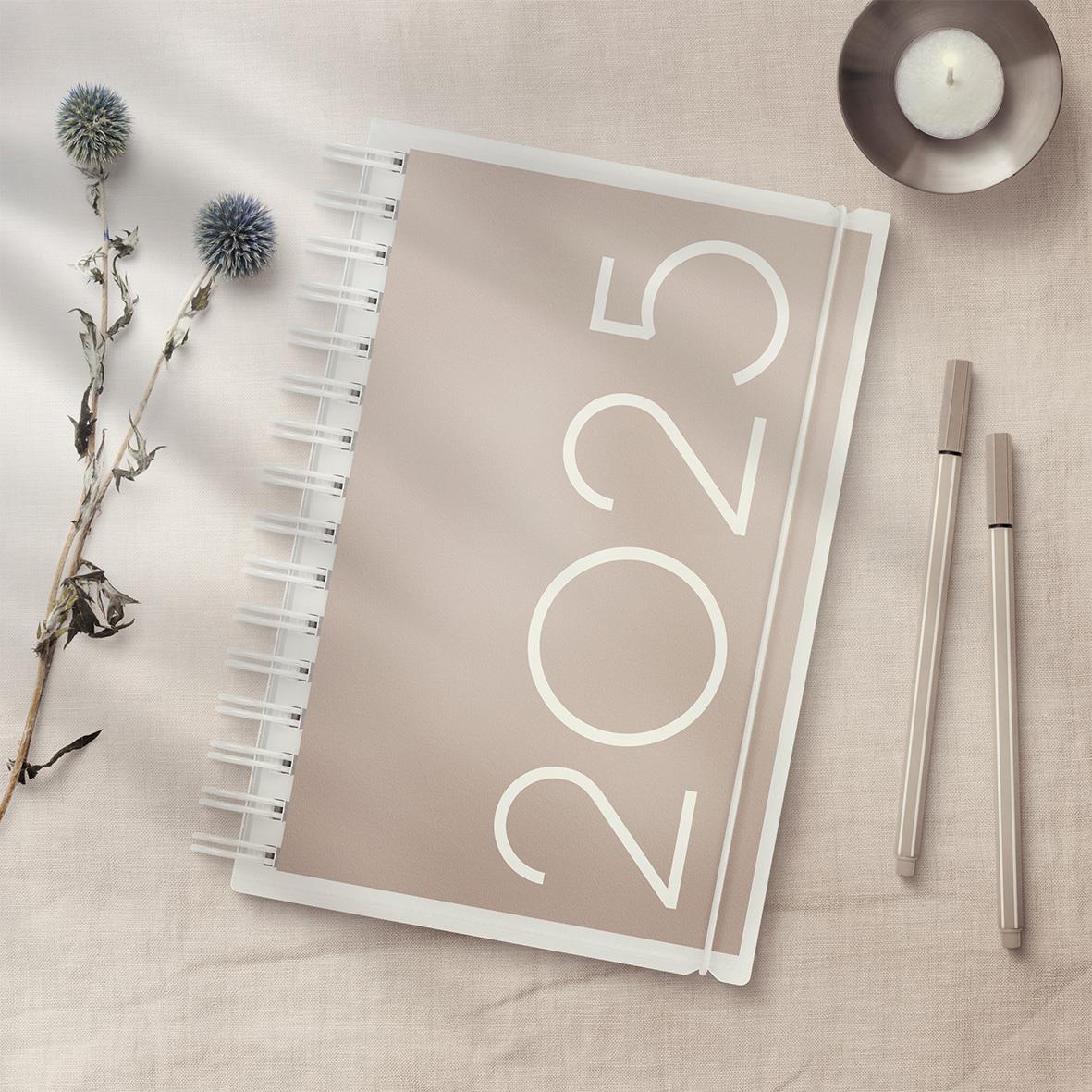 Årsdagbok 2025 med PP-omslag och två pennor på ljus bakgrund, dekorationer och ett ljus