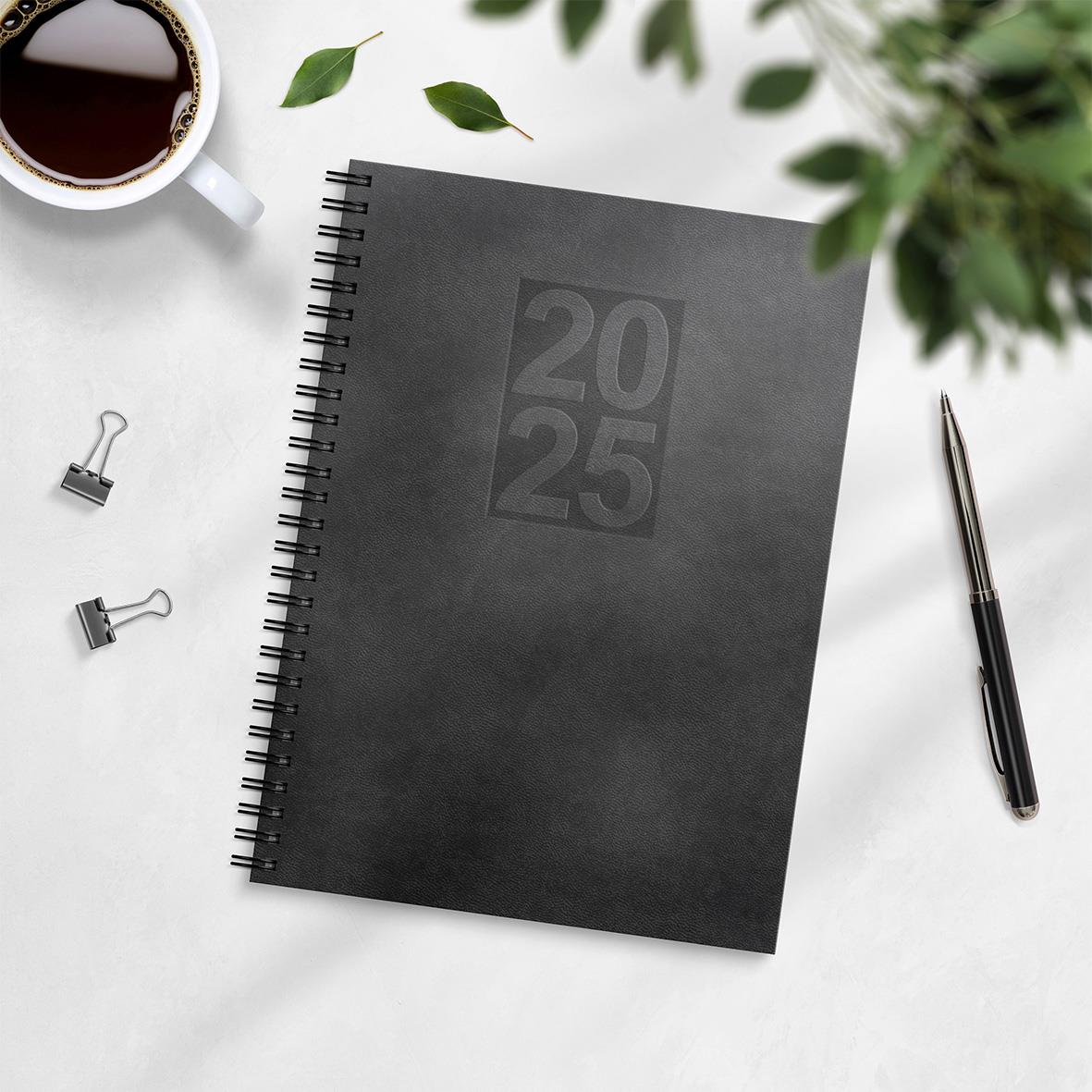 Svart almanacka för 2025 med spiralbindning och konstläderomslag, A5-storlek, på skrivbord med penna, koppar kaffe och gröna växter