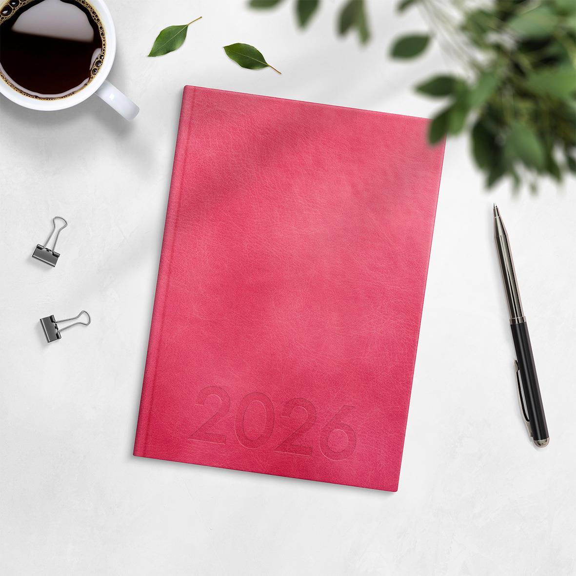 Rosa Almanacka Burde 1179 Weekly Konstläder Inbunden 2026 A5 på vit bakgrund med penna, koppar och gröna blad