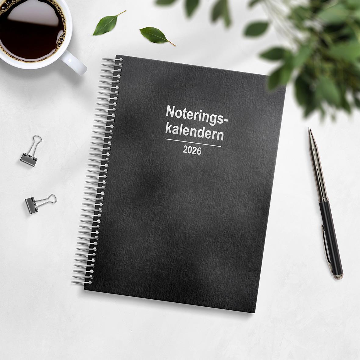 Svart noteringskalender för 2026 med spiralbindning och konstläderomslag, omgiven av kaffe, penna och gröna växter